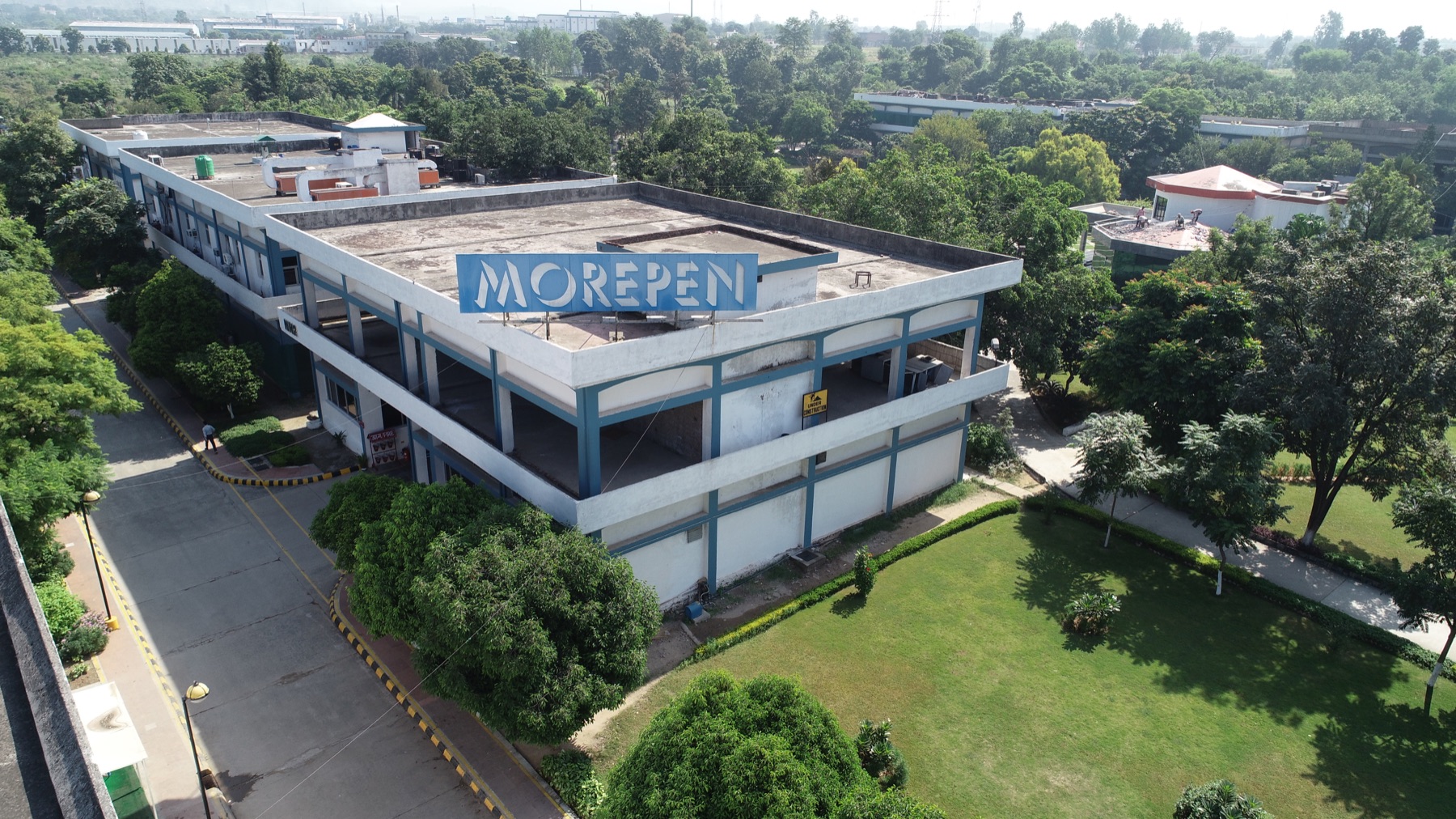 Morepen building with rooftop Morepen sign, surrounded by lawns and trees
